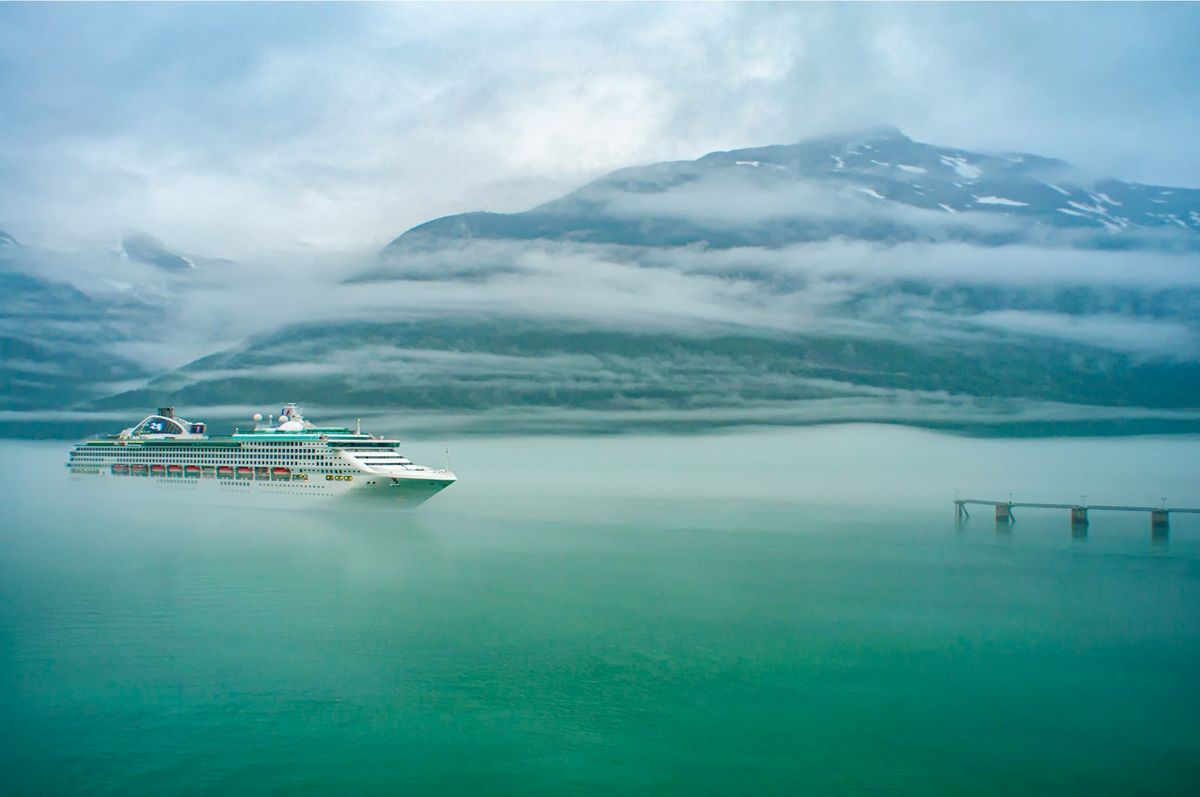Hvitt cruiseskip på vannet mellom fjell
