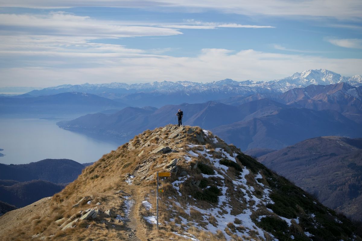 Fjellvandrer pa topp med panoramautsikt over fjell og vann