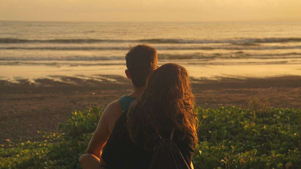 Par omfavner hverandre på stranden ved solnedgang
