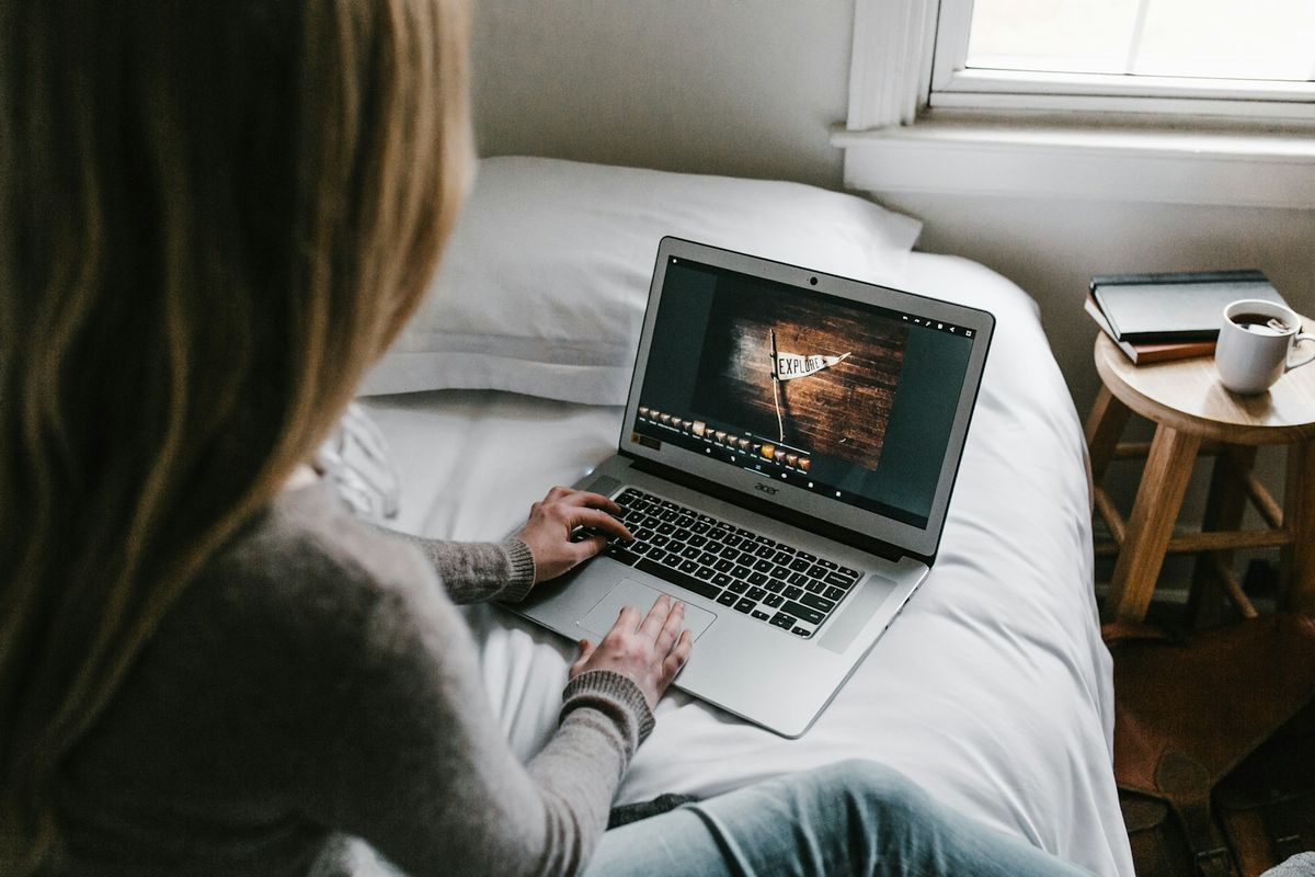 Kvinne som ser på video på bærbar datamaskin i en seng