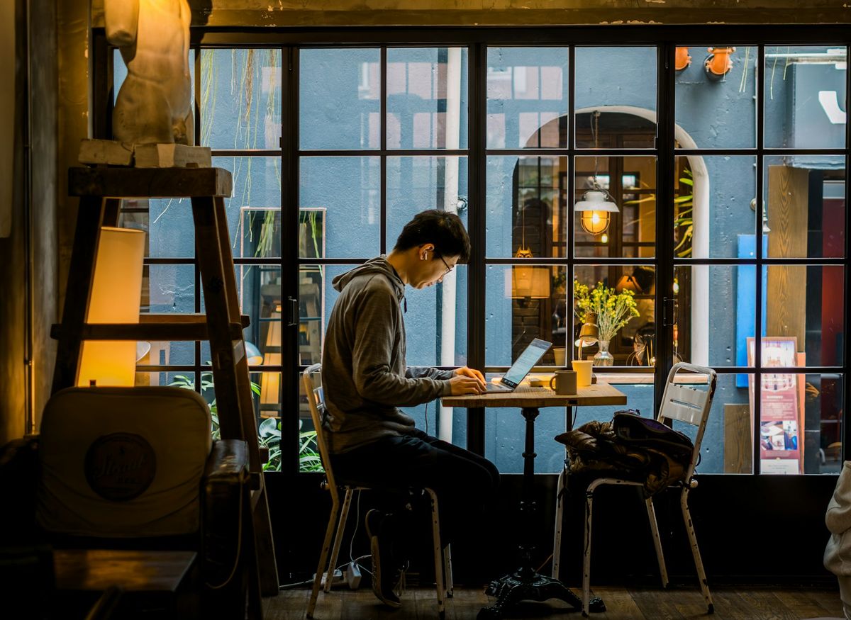 Mann som sitter konsentrert med bærbar datamaskin ved vinduet på en kafé